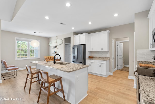 kitchen with light hardwood / wood-style floors, sink, appliances with stainless steel finishes, and an island with sink