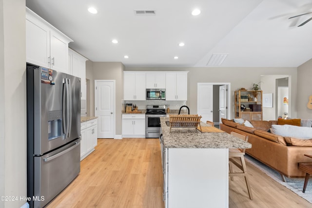 kitchen with white cabinets, a kitchen breakfast bar, light hardwood / wood-style flooring, an island with sink, and stainless steel appliances