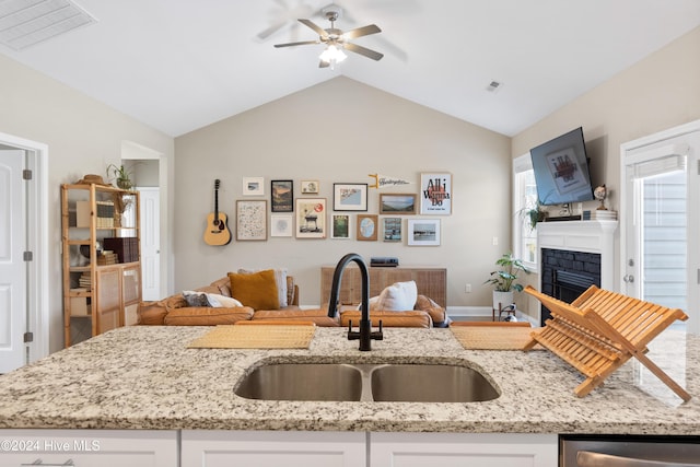 kitchen featuring light stone counters, ceiling fan, sink, white cabinets, and lofted ceiling