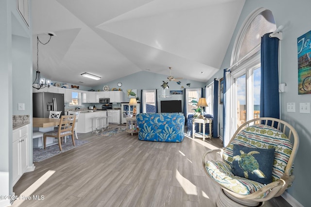 living room with ceiling fan with notable chandelier, light hardwood / wood-style flooring, and vaulted ceiling