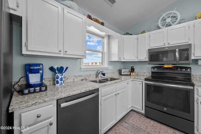 kitchen with sink, vaulted ceiling, light stone counters, white cabinetry, and stainless steel appliances