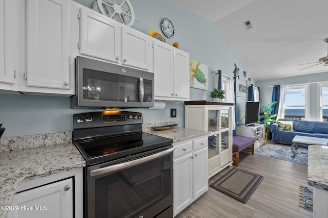 kitchen with white cabinets, vaulted ceiling, light wood-type flooring, light stone counters, and stainless steel appliances