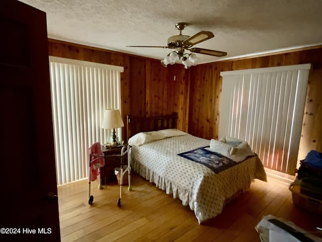 bedroom featuring ceiling fan, wooden walls, wood-type flooring, and a textured ceiling