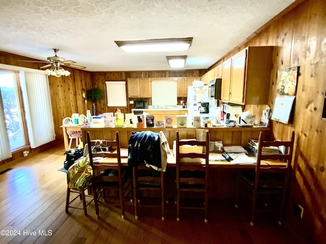 dining space with hardwood / wood-style flooring, ceiling fan, wood walls, and a textured ceiling