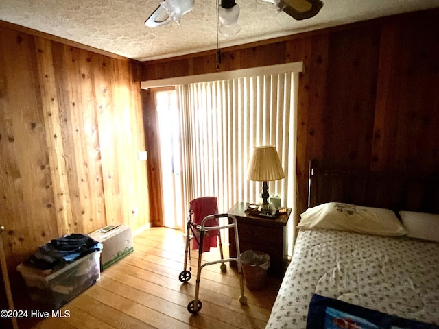 bedroom with a textured ceiling, light wood-type flooring, ceiling fan, and wood walls