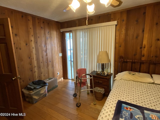 bedroom with ceiling fan, wood walls, and wood-type flooring