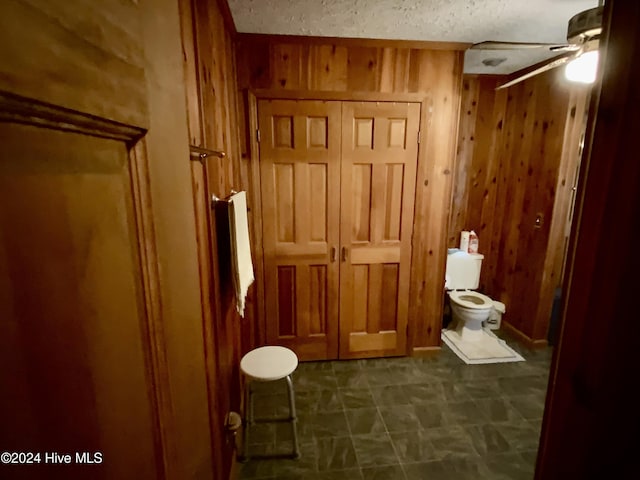 bathroom with ceiling fan, wood walls, and toilet