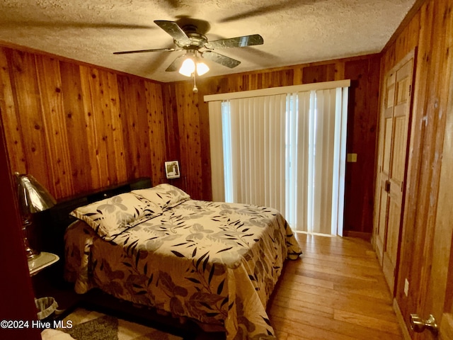 bedroom with a textured ceiling, ceiling fan, light hardwood / wood-style flooring, and wood walls