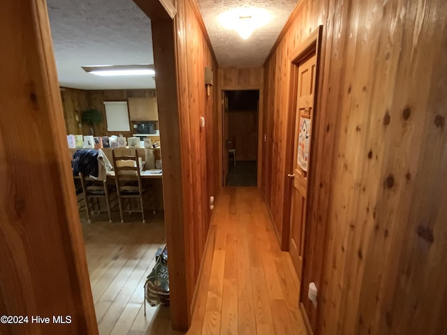 hallway featuring wooden walls, a textured ceiling, and light wood-type flooring