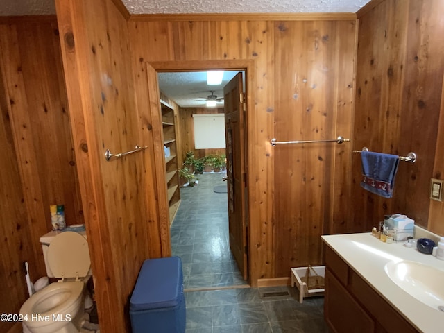 bathroom with vanity, wood walls, toilet, and a textured ceiling