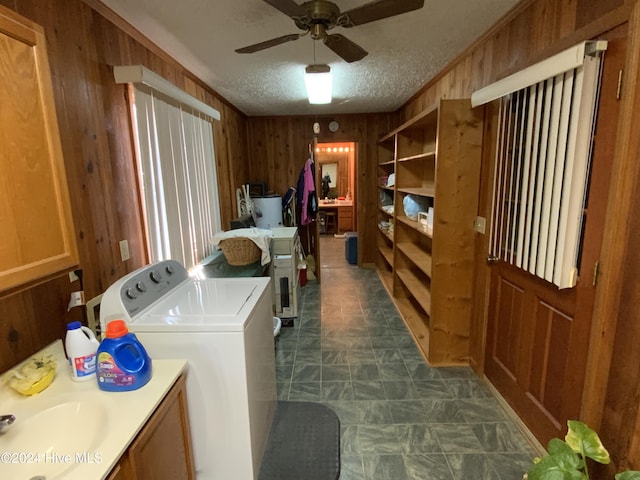 laundry area featuring a textured ceiling, ceiling fan, wooden walls, sink, and washing machine and clothes dryer