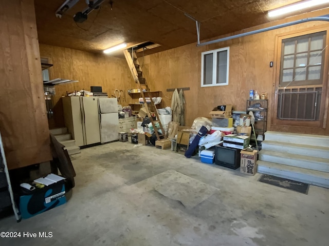 garage with wood walls, a garage door opener, white refrigerator, and stainless steel refrigerator