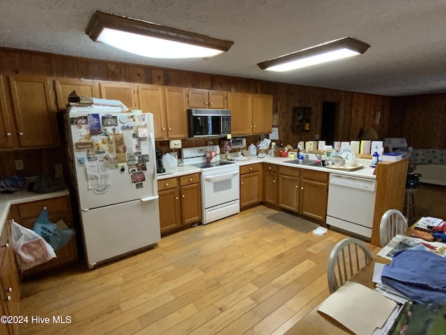 kitchen with a textured ceiling, wooden walls, light hardwood / wood-style floors, and white appliances