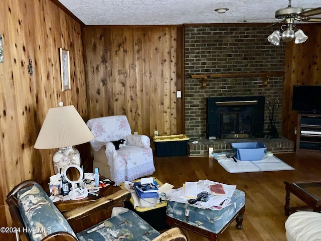 living room with hardwood / wood-style flooring, wood walls, a textured ceiling, and a brick fireplace