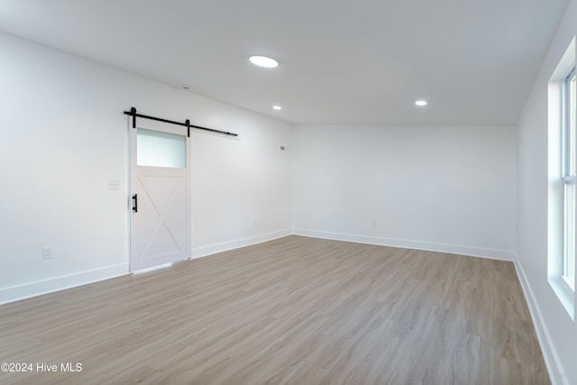 unfurnished room with a barn door, light hardwood / wood-style floors, a wealth of natural light, and lofted ceiling