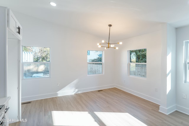 unfurnished room with an inviting chandelier and light hardwood / wood-style flooring