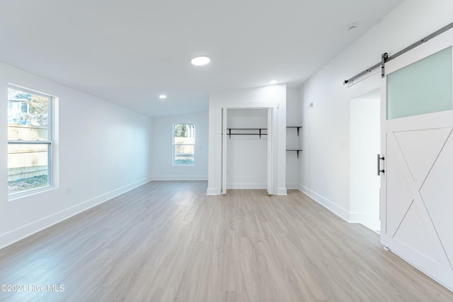 unfurnished room with plenty of natural light, a barn door, and light hardwood / wood-style flooring