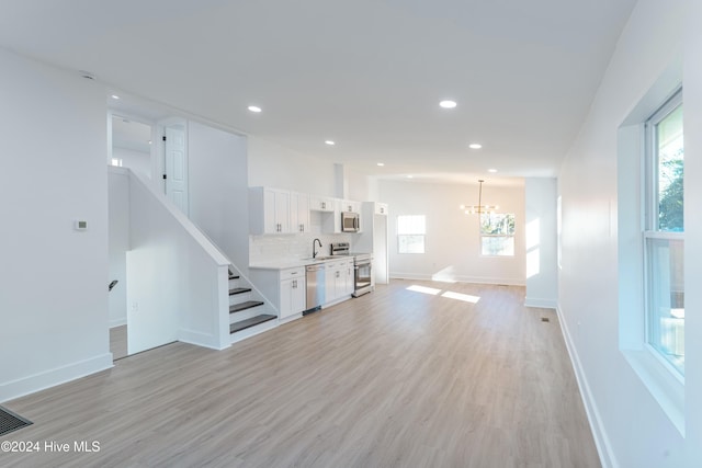 unfurnished living room with a notable chandelier, light wood-type flooring, sink, and a wealth of natural light