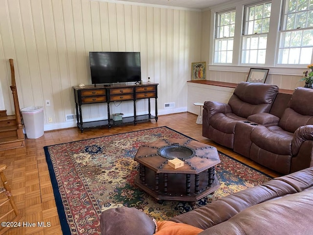 living room with crown molding, wooden walls, and parquet floors