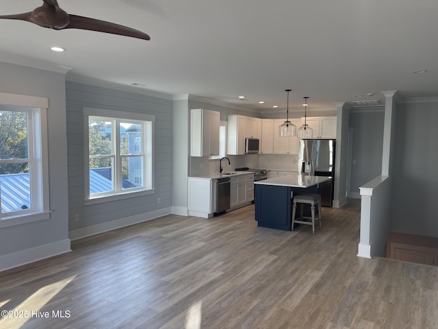 kitchen featuring a breakfast bar, white cabinetry, stainless steel appliances, a center island, and decorative light fixtures