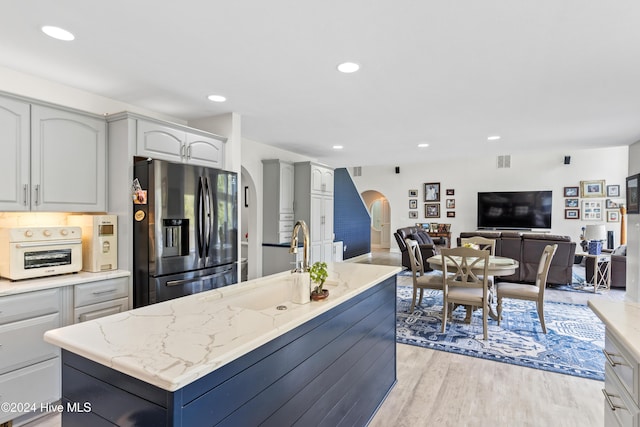 kitchen featuring light stone countertops, sink, a center island, stainless steel fridge, and light wood-type flooring