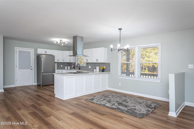 kitchen featuring island exhaust hood, stainless steel fridge, kitchen peninsula, pendant lighting, and white cabinets