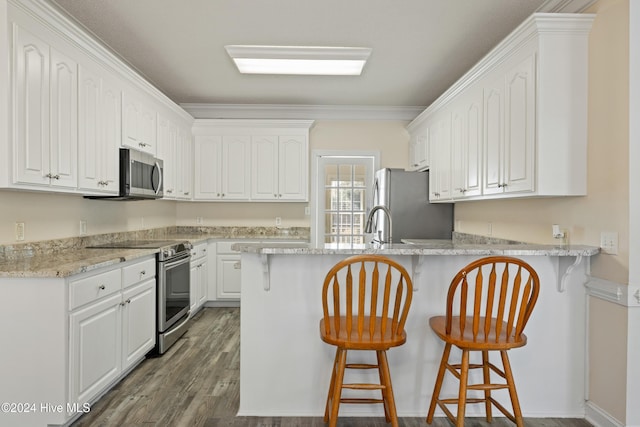 kitchen with appliances with stainless steel finishes, ornamental molding, dark wood-type flooring, white cabinetry, and a breakfast bar area