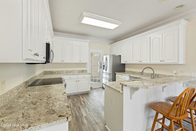 kitchen with kitchen peninsula, ornamental molding, stainless steel appliances, white cabinets, and light hardwood / wood-style floors