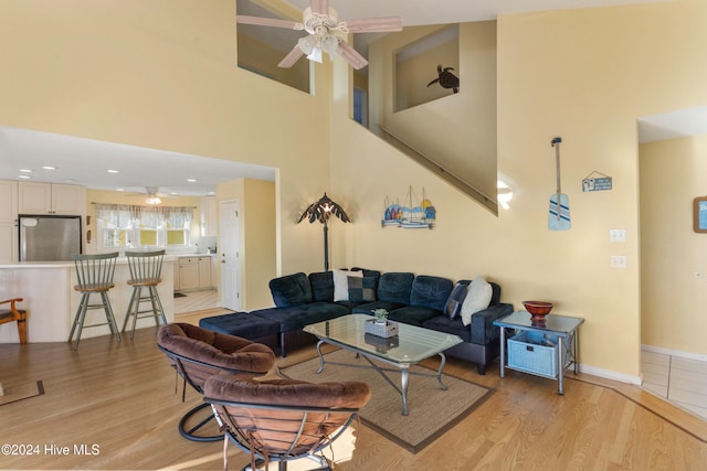 living room featuring ceiling fan, light hardwood / wood-style floors, and a high ceiling