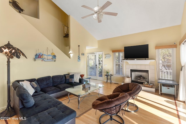 living room with hardwood / wood-style flooring, ceiling fan, a tile fireplace, and high vaulted ceiling