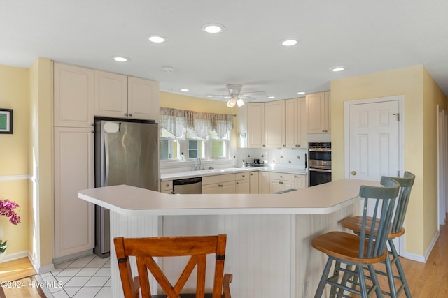 kitchen featuring a breakfast bar area, light hardwood / wood-style flooring, ceiling fan, tasteful backsplash, and stainless steel appliances