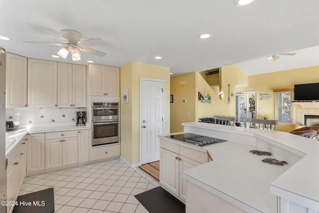 kitchen featuring ceiling fan, double oven, a tiled fireplace, decorative backsplash, and black electric stovetop