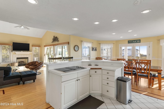 kitchen featuring ceiling fan, a tiled fireplace, black electric stovetop, white cabinets, and light wood-type flooring