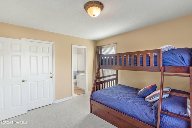 carpeted bedroom featuring ensuite bath and a textured ceiling