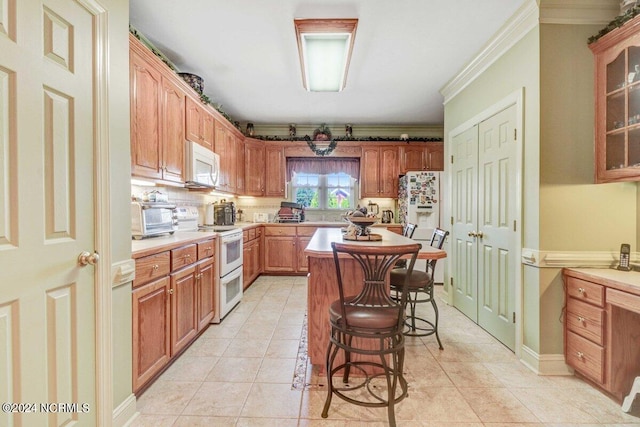 kitchen with light tile patterned flooring, white appliances, ornamental molding, a kitchen island, and a breakfast bar area