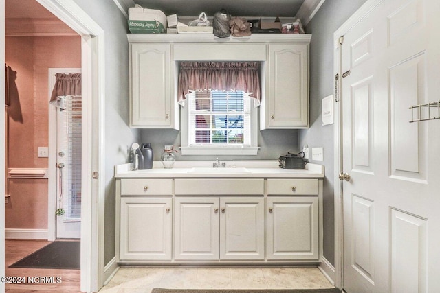 kitchen with light tile patterned flooring, white cabinetry, ornamental molding, and sink