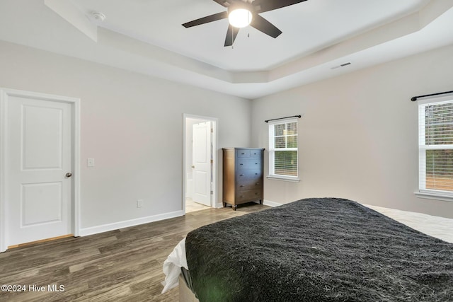 bedroom with a tray ceiling, ceiling fan, dark wood-type flooring, and ensuite bathroom