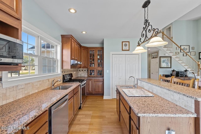 kitchen with sink, backsplash, an island with sink, appliances with stainless steel finishes, and light wood-type flooring