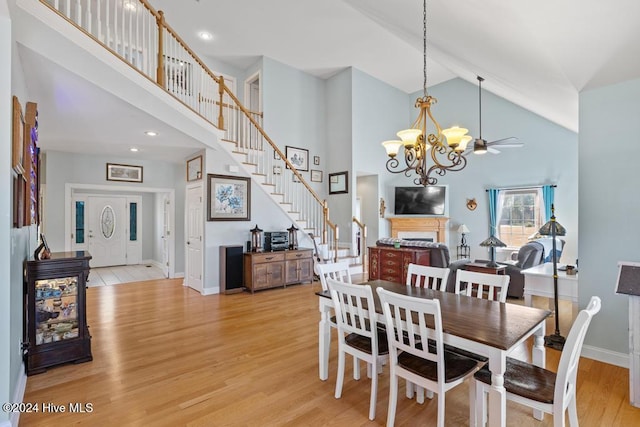 dining room with ceiling fan with notable chandelier, light wood-type flooring, and high vaulted ceiling