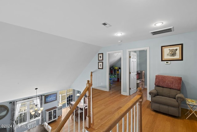 hallway with hardwood / wood-style flooring, an inviting chandelier, and vaulted ceiling