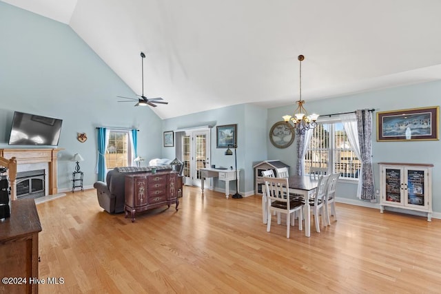 dining area with ceiling fan with notable chandelier, a healthy amount of sunlight, light wood-type flooring, and high vaulted ceiling