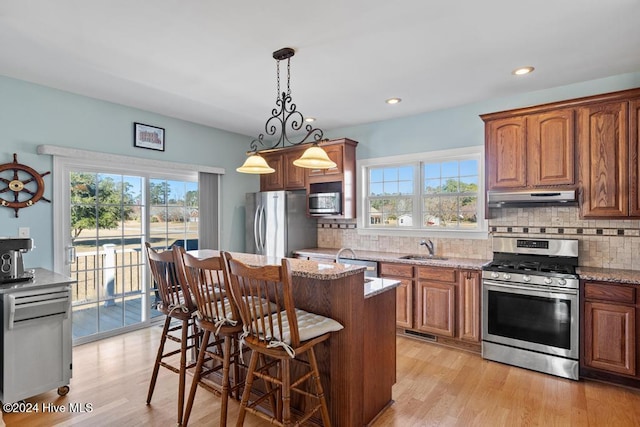 kitchen featuring light stone countertops, appliances with stainless steel finishes, sink, pendant lighting, and light hardwood / wood-style floors