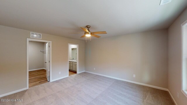 unfurnished bedroom with a walk in closet, ensuite bathroom, ceiling fan, and light colored carpet