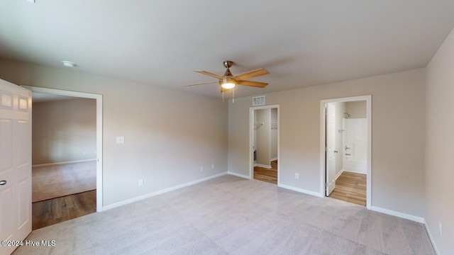 unfurnished bedroom featuring light carpet, ensuite bathroom, ceiling fan, a spacious closet, and a closet