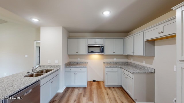 kitchen with white cabinets, sink, light hardwood / wood-style flooring, light stone counters, and stainless steel appliances