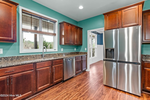 kitchen featuring wood-type flooring, stainless steel appliances, dark stone counters, and sink