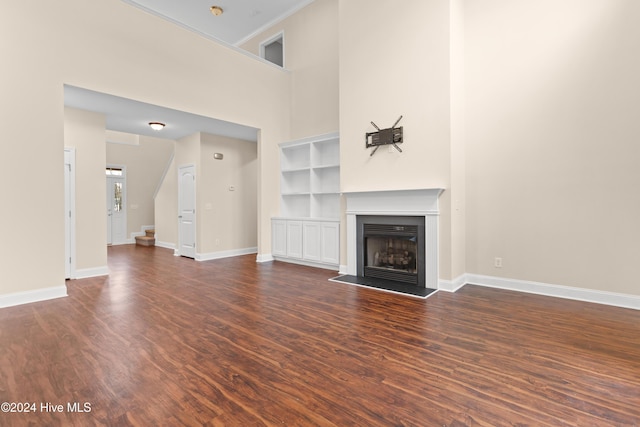 unfurnished living room with built in shelves, dark hardwood / wood-style flooring, and a towering ceiling