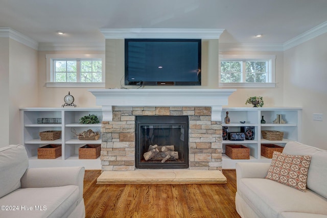 living room with wood-type flooring, a stone fireplace, plenty of natural light, and ornamental molding