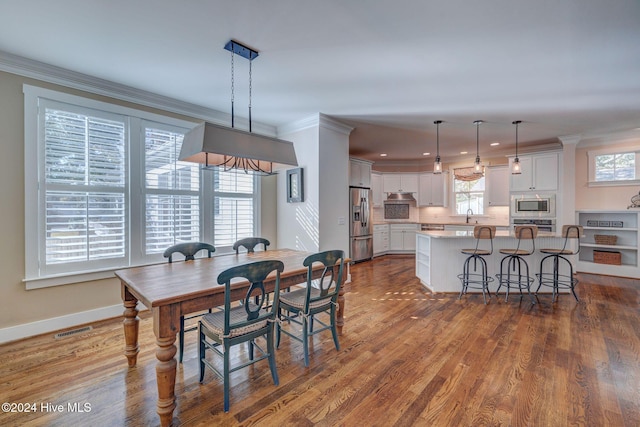 dining space featuring crown molding, sink, a healthy amount of sunlight, and wood-type flooring