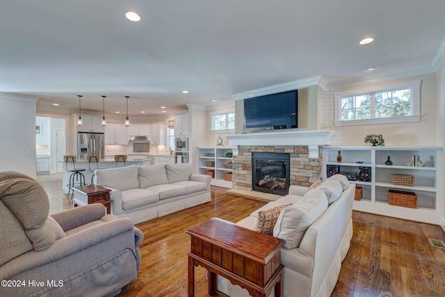 living room featuring a stone fireplace, crown molding, plenty of natural light, and hardwood / wood-style flooring